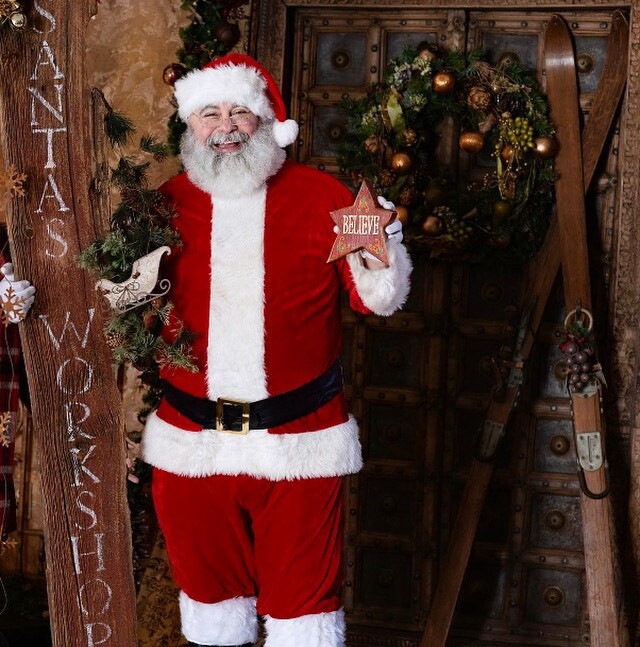 Professional Santa in Charlotte NC welcoming guests from a decorated holiday doorway